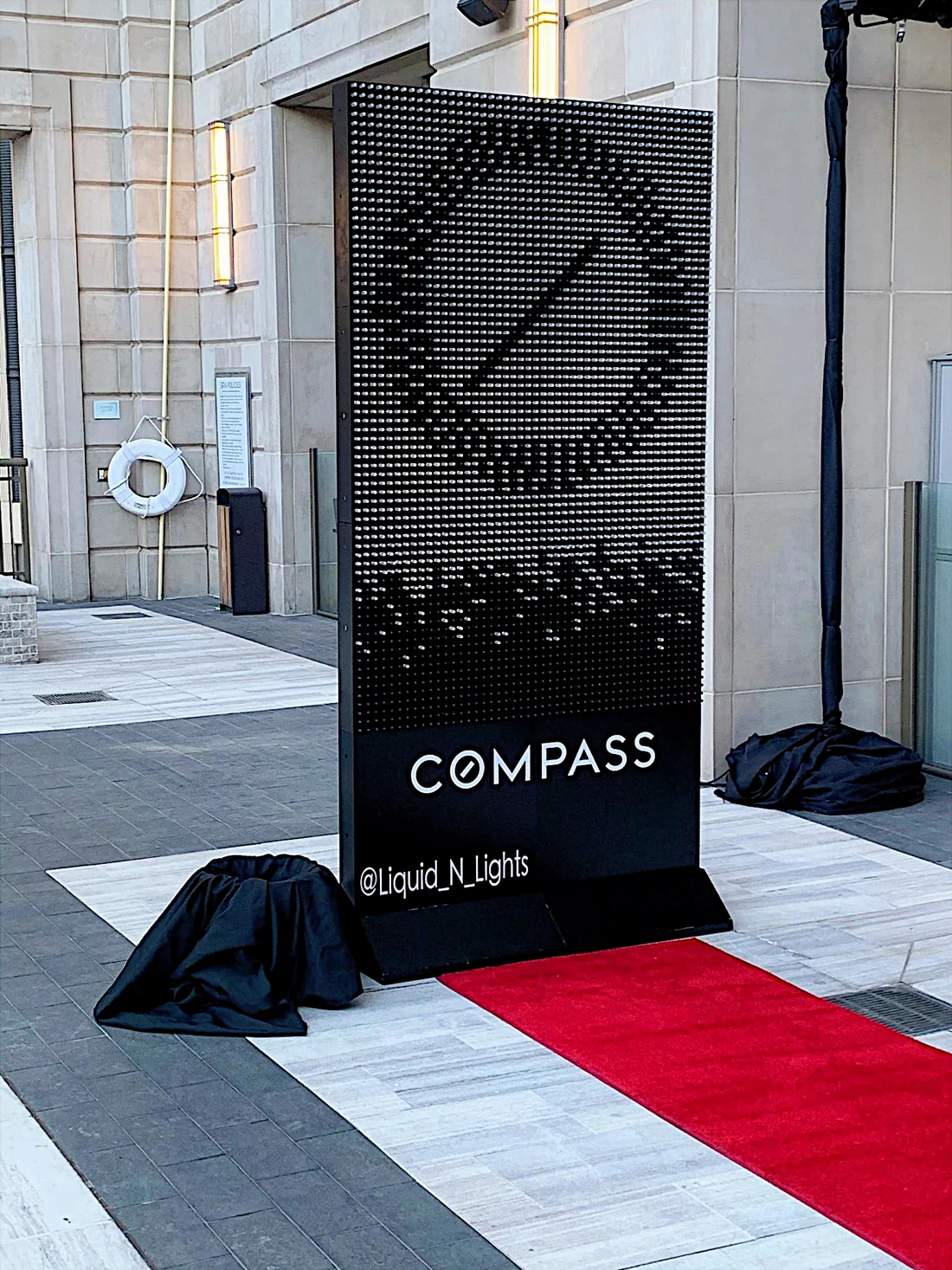 Compass-branded illuminated pipette wall installed at an event entrance